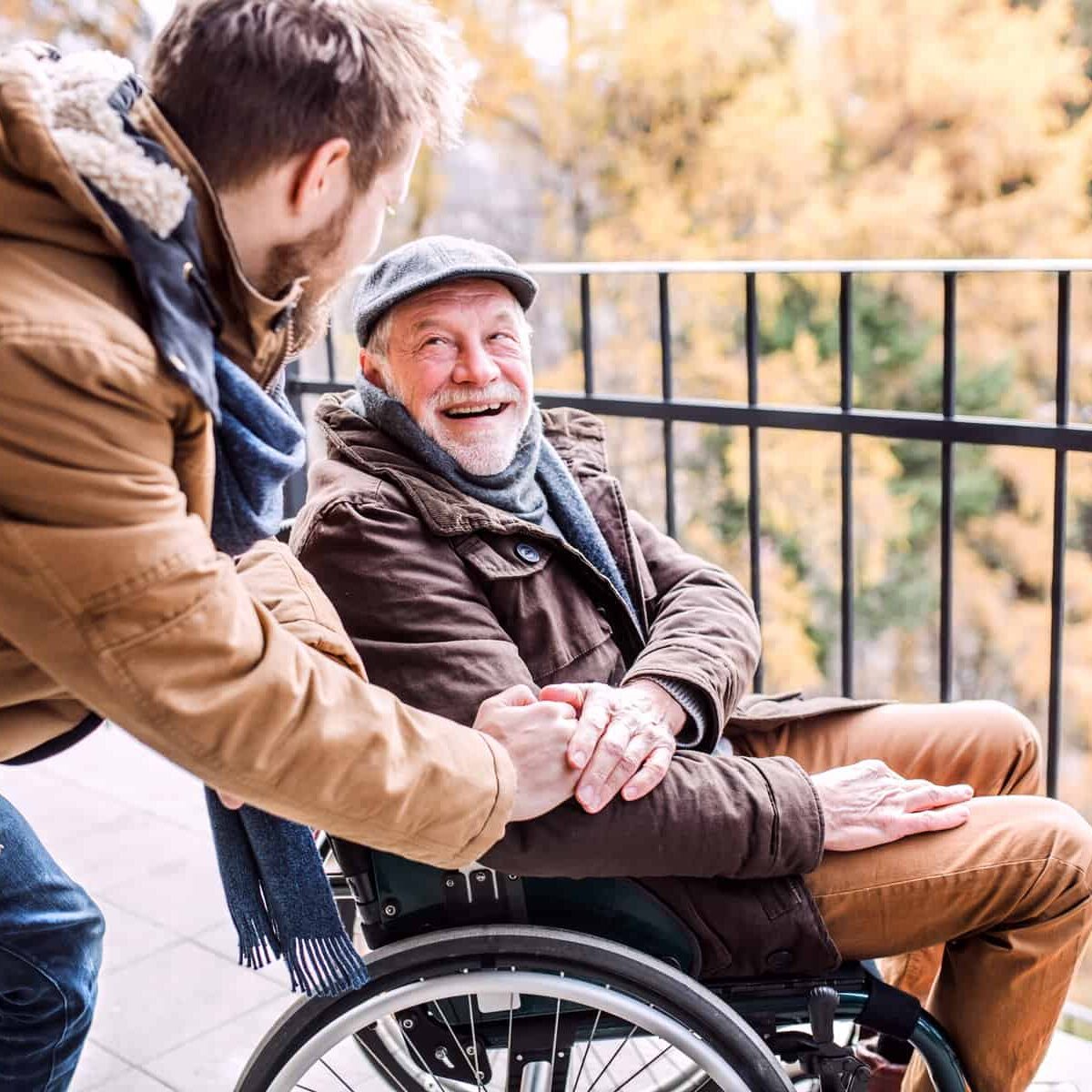 Father in wheelchair and young son on a walk. A carer assisting disabled senior man.